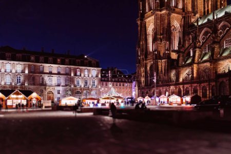 Téléchargez les photos : Enchanteresse Place de Château ornée de la cathédrale Notre-Dame de Strasbourg illuminée au crépuscule pendant le Marché de Noël, alors que les piétons explorent l'ambiance festive - en image libre de droit