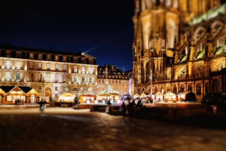 Foto de Majestuosa Plaza de Chateau con la iluminada Catedral de Notre-Dame de Estrasburgo al atardecer durante el Mercado de Navidad con peatones descubriendo el lugar - Imagen libre de derechos