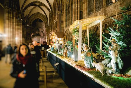 Foto de Vista desenfocada de los espectadores admiran un detallado pesebre que representa la natividad dentro de la histórica Notre-Dame de Strasbourg, iluminada en un ambiente sereno. - Imagen libre de derechos
