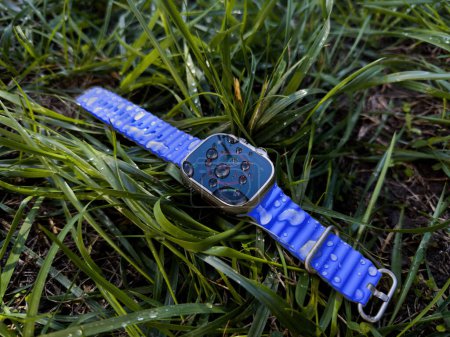 Foto de París, Francia - 23-sep-2022: La imagen muestra un Apple Watch Ultra 2 perdido tumbado sobre hierba verde húmeda, mostrando las capacidades resistentes al agua de los relojes después de una lluvia - correa azul - Imagen libre de derechos