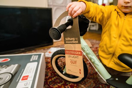 Téléchargez les photos : Munich, Allemagne - Apr 8, 2023 : Un jeune enfant tient une étiquette de récompense sur un vélo Puky équilibre à l'intérieur d'une pièce, signifiant les jouets haut de gamme. - en image libre de droit