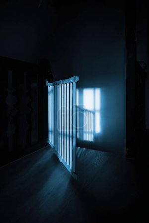 Foto de Un primer plano de una barrera de escalera de madera en una casa de lujo, bañada por los rayos del sol. El pasillo oscuro brilla con calidez, creando un impresionante contraste visual - Imagen libre de derechos