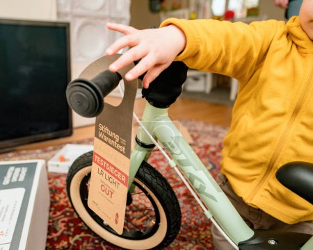 Foto de Múnich, Alemania - 8-abr-2023: Un niño pequeño está desempacando una etiqueta de premio en una bicicleta Puky de equilibrio dentro de una habitación, lo que significa que los juguetes de alta calificación - Imagen libre de derechos