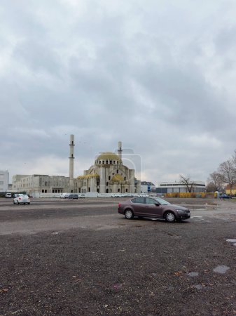 Téléchargez les photos : Strasbourg, Frna ce- Jan 7, 2024 : Une voiture solitaire est garée dans un terrain spacieux devant une mosquée inachevée sous un ciel nuageux, représentant une journée calme dans un cadre urbain - en image libre de droit