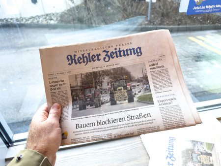 Téléchargez les photos : Kehl, Allemagne - 9 janvier 2024 : une personne tient un journal intitulé Kehler Zeitung avec un titre sur les agriculteurs bloquant les rues, révélant une manifestation locale ou un événement important. - en image libre de droit