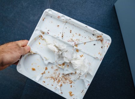 Photo for A male hand holds an empty plastic cake tray above a blue background, showcasing small traces and crumbs, remnants of an afterparty - Royalty Free Image
