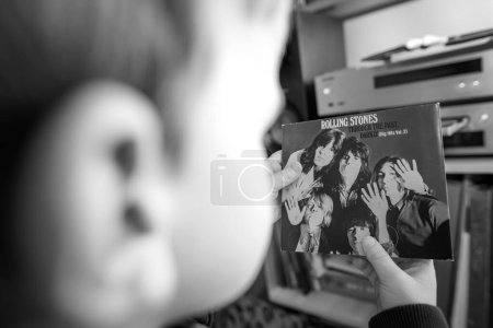 Photo for Paris, France - Jan 18, 2024: A toddler is seen holding the Rolling Stones Through the Past, Darkly SACD disk in a living room with a high-end hi-fi system and luxury speakers, nurturing an - Royalty Free Image
