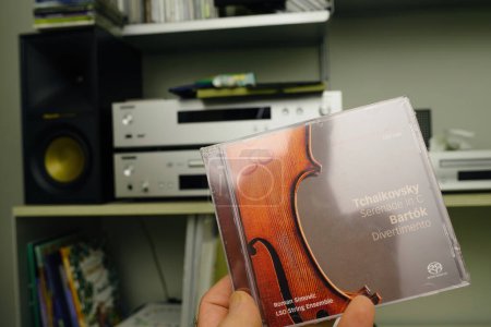 Téléchargez les photos : Paris, France - 21 janv.2024 : Une main masculine tient délicatement un disque ACD de Roman Simovic, avec l'Ensemble à cordes LSO jouant des compositions Tchaïkovski et Bartok, contre une chaîne hi-fi - en image libre de droit