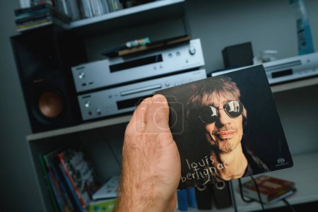 Foto de París, Francia - 21 de enero de 2024: Una mano masculina sostiene delicadamente el álbum de SACD of Louis Bertignacs Longtemps, una preciada joya audiófila, sobre un fondo temático audiófilo - Imagen libre de derechos
