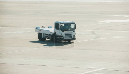Photo for Frankfurt, Germany - Oct 2, 2015: A Scania airport tug vehicle by Swissport drives on the tarmac, its cargo services empty, under the bright glare of the sun. - Royalty Free Image