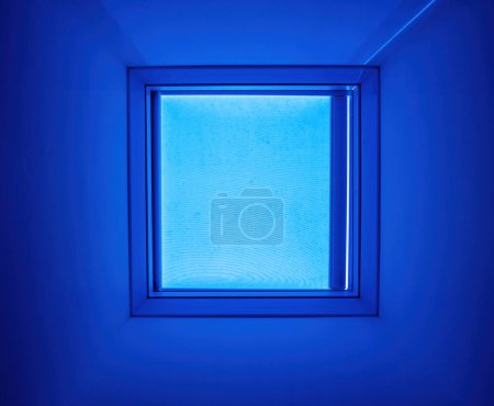 Téléchargez les photos : Une lueur bleue surréaliste infuse cette pièce, provenant d'une lucarne carrée, ajoutant une sensation unique et futuriste à l'espace - en image libre de droit