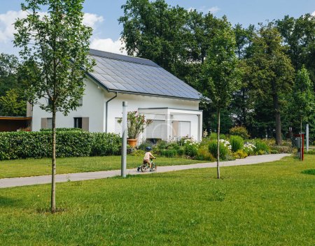 Téléchargez les photos : Un vélo d'enfant le long d'un chemin dans un quartier de banlieue luxuriante, avec une maison moderne ornée de panneaux solaires dans le contexte serein. - en image libre de droit