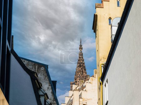 Téléchargez les photos : Vue d'une flèche historique de la cathédrale Notre-Dame de Strasbourg s'élevant majestueusement au-dessus de toits pittoresques sous un ciel bleu clair, dans un cadre urbain serein. - en image libre de droit