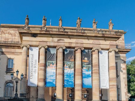 Foto de Estrasburgo, Francia - 2 de julio de 2023: El edificio principal de la Ópera Nacional del Rin en Estrasburgo, Alsacia, con estatuas en la parte superior, frente a un cielo azul claro. - Imagen libre de derechos