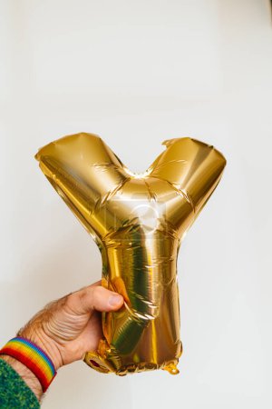 Foto de Una mano masculina sostiene un magnífico globo de helio inflable dorado en la forma de la letra Y. Esta impresionante fuente gold foil balloon es perfecta para invitaciones, tarjetas de felicitación, San Valentín - Imagen libre de derechos