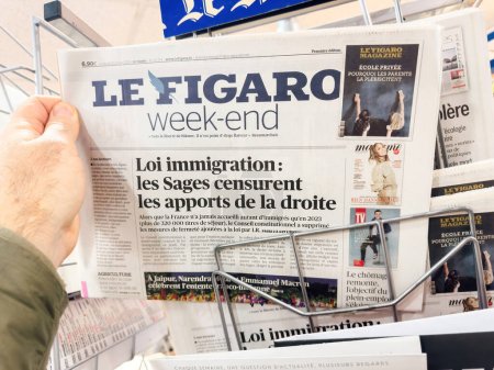 Foto de París, Francia - 26 de enero de 2024: Punto de vista de un hombre que sostiene el último periódico Le Figaro con la Loi Immigration promulgada por Emmanuel Macron y las disparidades sociales que crea - Imagen libre de derechos