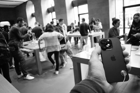Photo for Paris, France - Sep 22, 2023: A man holds the latest Apple iPhone 14 Pro inside an Apple store, surrounded by curious customers who are chatting and coming to see the new smartphones. The image is in - Royalty Free Image