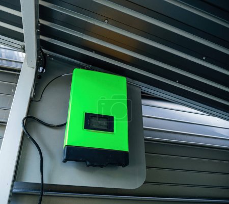 Téléchargez les photos : Un onduleur solaire vert industriel installé sur un mur de garage métallique, exploitant l'énergie renouvelable de la lumière du soleil. - en image libre de droit