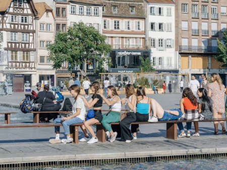 Téléchargez les photos : Strasbourg, France - 2 juil. 2023 : Groupe de jeunes filles femmes socialisant et assises sur des bancs près d'une fontaine par une journée chaude et ensoleillée. Place Kleber Strasbourg - en image libre de droit