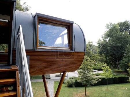 Téléchargez les photos : Unique maison en bois avec de grandes fenêtres, située dans un parc verdoyant, surélevée sur pilotis. - en image libre de droit