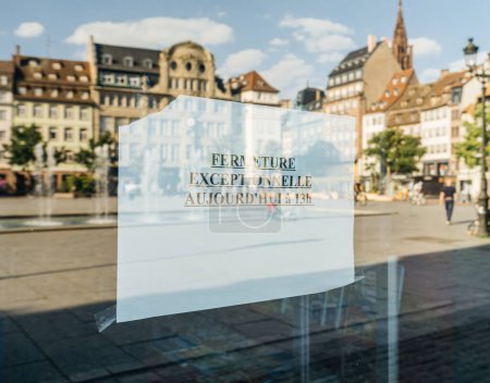Foto de Reflejo de una plaza de la ciudad y edificios en un cartel de cierre inesperado en francés. - Imagen libre de derechos