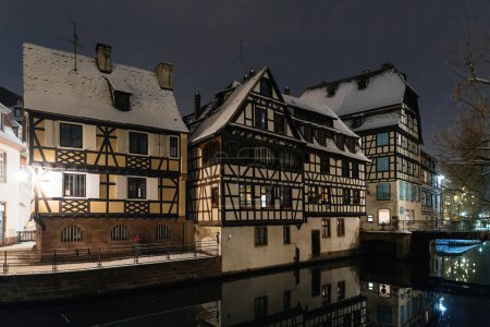 Photo for Timber framed houses reflecting in the canal, adorned with snow on a tranquil night - Royalty Free Image
