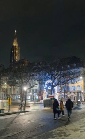 Foto de Una noche fría en el corazón de Estrasburgo, donde la gente camina a lo largo de la calle peatonal iluminada, con la majestuosa Catedral de Notre-Dame en vista - Imagen libre de derechos