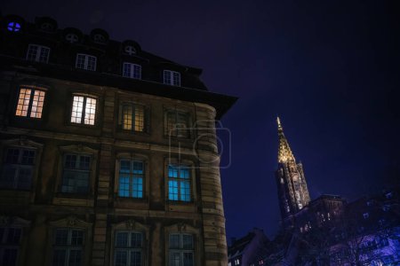 Téléchargez les photos : Une vue imprenable sur un immeuble de luxe avec une fenêtre éclairée, sur fond de cathédrale Notre-Dame sous un ciel bleu clair - en image libre de droit