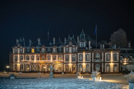 Téléchargez les photos : Vue de face d'un grand manoir historique château de Pourtales, orné de lumières festives lors d'une soirée enneigée - en image libre de droit