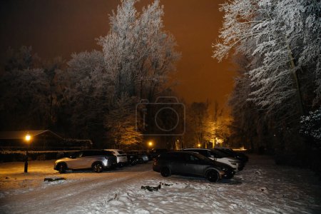 Téléchargez les photos : Strasbourg, France - 19 déc. 2022 : Véhicules chargés de neige garés sous un ciel nocturne brumeux avec des lumières ambiantes en arrière-plan - en image libre de droit