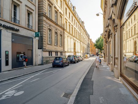 Foto de Estrasburgo, Francia - 2 de julio de 2023: Una mujer con un niño pasea por un lado de la calle, mientras que en el lado opuesto, un hombre retira dinero del cajero automático del BNP Paribas, capturando la dinámica vida callejera - Imagen libre de derechos