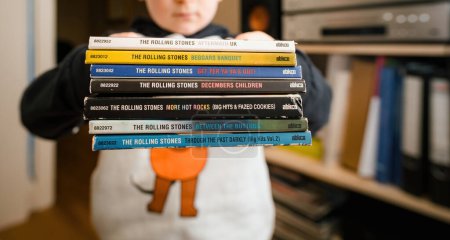 Photo for Paris, France - Jan 17, 2024: Toddler holding stack of classic Rolling Stones SACD Super Audiop CD albums in his hands. - Royalty Free Image