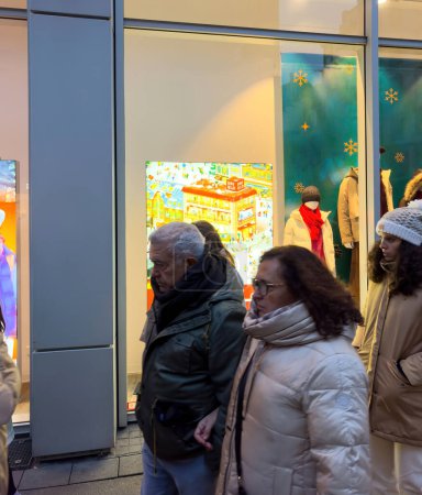 Téléchargez les photos : Les piétons marchent avec impatience vers les magasins UNIQLO Vitrine de Noël, attirés par les expositions festives et les offres de vacances, créant une scène animée sur la rue commerçante animée. - en image libre de droit