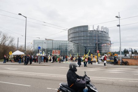 Foto de Estrasburgo, Francia - 6 de febrero de 2024: Hombre en motocicleta frente a manifestantes que bloquean la entrada del Parlamento Europeo, protestan contra las normas alimentarias importadas y los nuevos OMG - Imagen libre de derechos