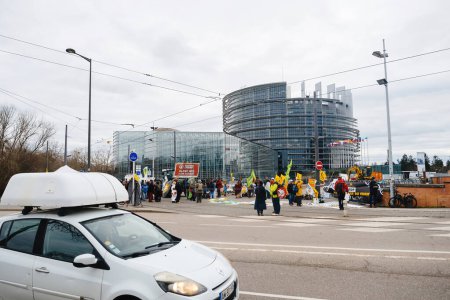 Téléchargez les photos : Strasbourg, France - 6 février 2024 : Manifestation de foule avec drapeaux à l'entrée du Parlement européen contre les normes alimentaires importées et les nouveaux OGM - en image libre de droit