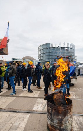 Téléchargez les photos : Strasbourg, France - 6 février 2024 : Un grand feu réchauffe les manifestants alors que des tracteurs bloquent l'entrée du Parlement, protestant contre les normes alimentaires importées et les nouveaux OGM - en image libre de droit
