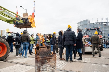 Téléchargez les photos : Strasbourg, France - 6 février 2024 : Des manifestants avec des tracteurs bloquent l'entrée du Parlement européen, utilisant le feu pour se réchauffer, protestant contre les aliments importés avec des normes plus basses et de nouveaux OGM - en image libre de droit