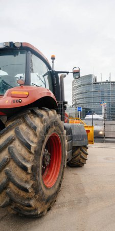 Foto de Estrasburgo, Francia - 6 de febrero de 2024: Gran tractor rojo frente al Parlamento Europeo, símbolo de protesta contra los alimentos importados con estándares más bajos y nuevos OMG - Imagen libre de derechos