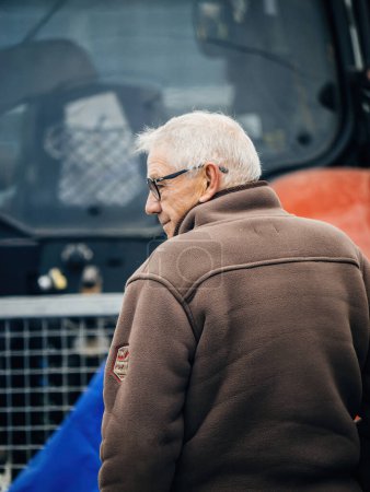 Photo for Strasbourg, France - Feb 6, 2024: Rear view of senior man in front of tractor blocking entrance to European Parliament, protesting against imported food with lower standards and new GMOs - Royalty Free Image