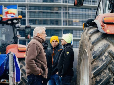 Photo for Strasbourg, France - Feb 6, 2024: Adults and senior farmers talk as protesters with tractors block EU Parliament entrance, protesting against imported food with lower standards and new GMOs - Royalty Free Image
