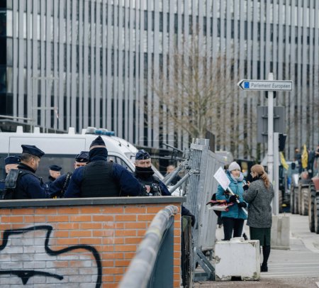Foto de Estrasburgo, Francia - 6 de febrero de 2024: La policía vigila a los manifestantes a través de la valla de seguridad mientras los tractores bloquean la entrada del Parlamento Europeo, protestando contra las normas alimentarias importadas y los nuevos OMG - Imagen libre de derechos