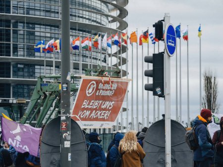 Foto de Estrasburgo, Francia - 6 de febrero de 2024: Manifestantes con tractores bloquean la entrada al Parlamento Europeo, con pancarta en alemán, protestando contra alimentos importados con estándares más bajos y nuevos OMG - Imagen libre de derechos