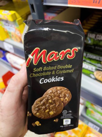 Photo for Dortmund, Germany - Feb 19, 2022: POV male hand holding package pack with Mars Soft baked double chocolate and caramel cookies with shelves in supermarket in background - Royalty Free Image