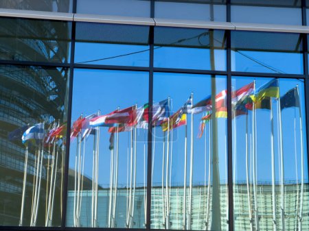 Foto de Estrasburgo, Francia - 4 de marzo de 2022: Reflexión en la ventana de la bandera de Ucrania junto a todas las banderas de los miembros de la Unión Europea frente al Parlamento Europeo - cielo azul claro y pacífico - Imagen libre de derechos