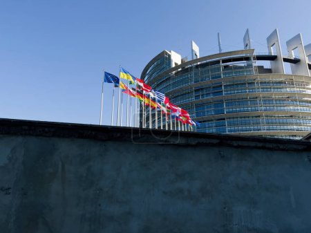 Foto de Estrasburgo, Francia - 4 de marzo de 2022: ondeando la bandera de Ucrania junto a todas las banderas de los miembros de la Unión Europea frente al Parlamento Europeo - cielo azul claro y pacífico - Imagen libre de derechos