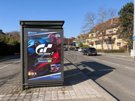 Téléchargez les photos : Strasbourg, France - 8 mars 2022 : Scène de rue strasbourgeoise avec gare routière contenant de la publicité pour le nouveau jeu vidéo GT Gran Turismo 7 - voitures en arrière-plan - en image libre de droit