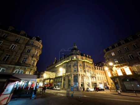 Téléchargez les photos : Strasbourg, France - 31 déc. 2023 : Une rue urbaine la nuit remplie de bâtiments illuminés, mettant en valeur une atmosphère urbaine vibrante à Strasbourg - en image libre de droit