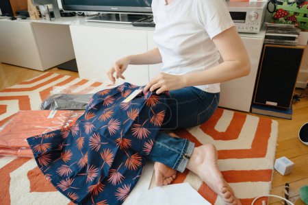 Téléchargez les photos : Lyon, France - 27 déc. 2023 : Jeune femme assise par terre à la maison, vêtements de déballage achetés en ligne - en image libre de droit