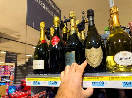 Foto de Lyon, Francia - 27 de diciembre de 2023: Una mano masculina busca una botella de champán Dom Perignon caro a un precio de 3023.90 en un pasillo de supermercado - Imagen libre de derechos