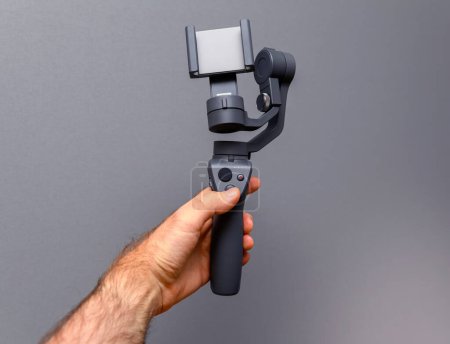 Téléchargez les photos : Une main masculine saisit fermement un stabilisateur de caméra sur un fond gris neutre, prêt pour un tournage régulier et en douceur - en image libre de droit